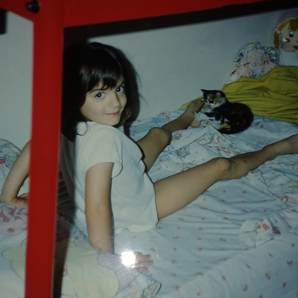 Glen as a child on her bed, with a black cat