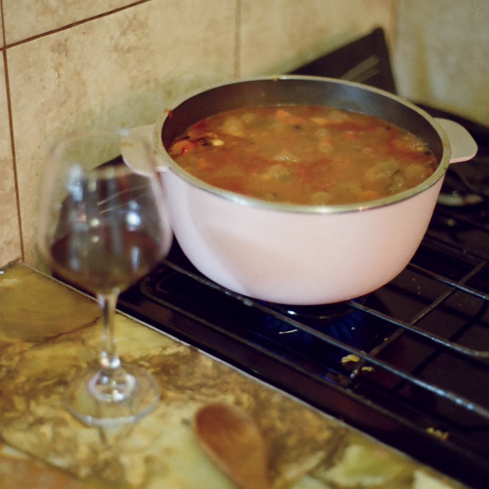 A pot of stew on the stove next to a glass of red wine